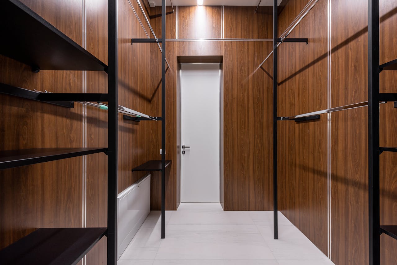 Empty black shelves and racks placed near brown walls in walk in closet with minimalist interior and white door at home
